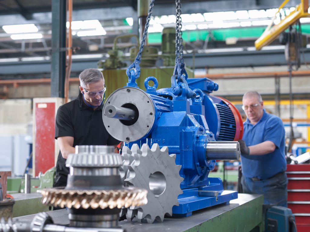 En stor hydraulpump och två personer som jobbar på den